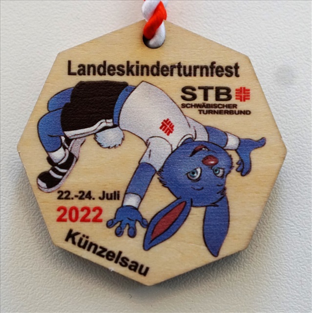 Die achteckige Teilnehmerplakette fr das STB Landeskinderturnfest 2022 aus Holz zeigt Turni beim Salto rckwrts